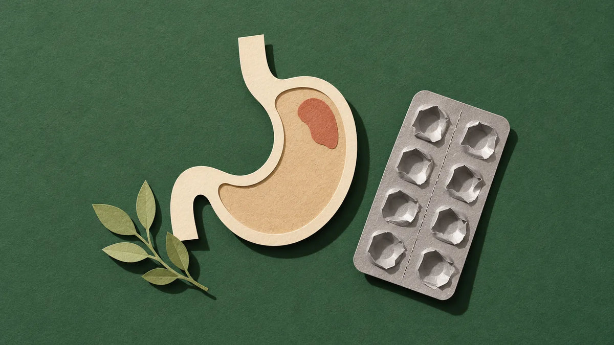 A paper-cut stomach with a small warm patch near the top, beside an empty pill blister strip: the burn that outlasts the treatment